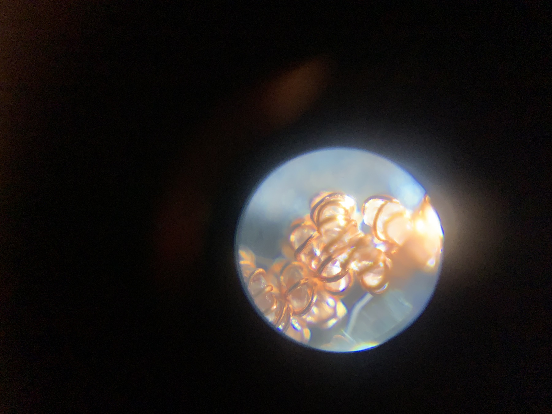 A copper-wrapped multi-ply artificial muscle viewed through a microscope, with its coils lit orange and blue
